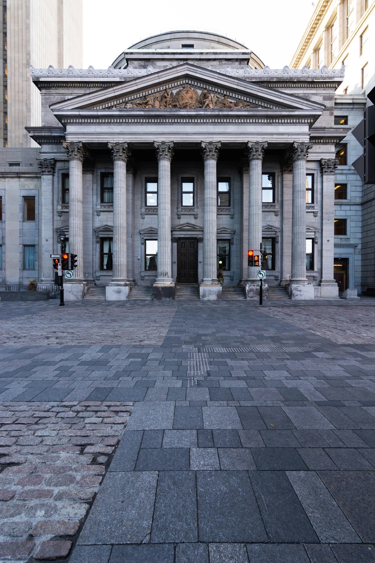 Fachada neoclásica de un banco, con columnas corintias y frontón, vista desde una plaza empedrada